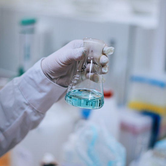 Gloved hand holding glass flask with blue liquid in a chemical synthesis lab